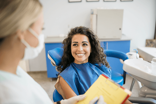 Dental patient smiling during a consultation, seated in a modern clinic with blue cabinetry—highlighting a welcoming environment for hybrid denture evaluations and personalized care.